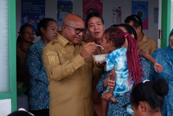 
					Penjabat Bupati Yapen, Welliam Manderi menyuapi anak saat kunjungan di Pustu Anotorei, Selasa 19 Desember 2023. (KabarPapua.co/Ainun Faathirjal)