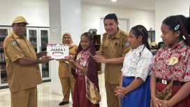 Plt Kepala Dinas Perpustakanaan dan Kearsipan Kabupaten Jayawijaya, Heribertus Mabel saat menyerahkan hadiah kepada Juara 1 Lomba Membaca Cerita Rakyat Papua. (Foto dok: Kominfo Jayawijaya)
